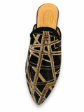 Black babouche with intersecting gold geometric lines and a pointed toe on a white background.