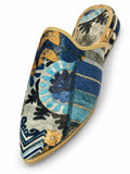 Blue and green patterned babouche with floral motifs, geometric blocks and gold-tone braided edging on a white background.