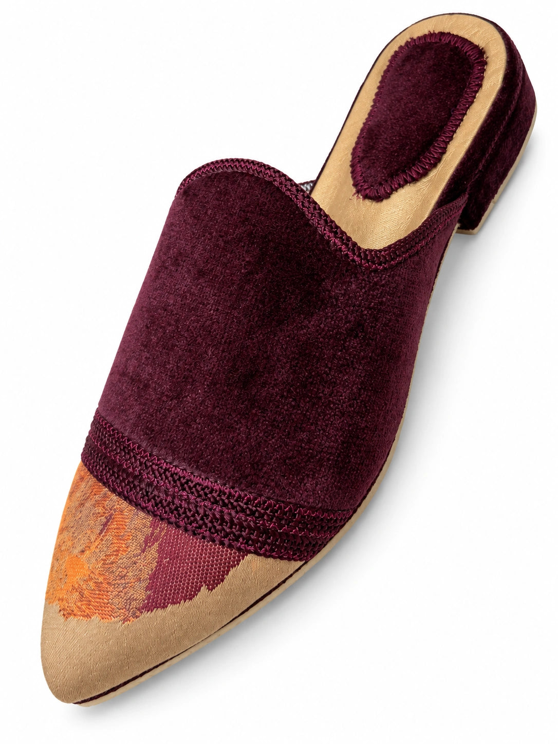Burgundy babouche with an orange and burgundy patterned toe, braided trim and an open back on a white background.