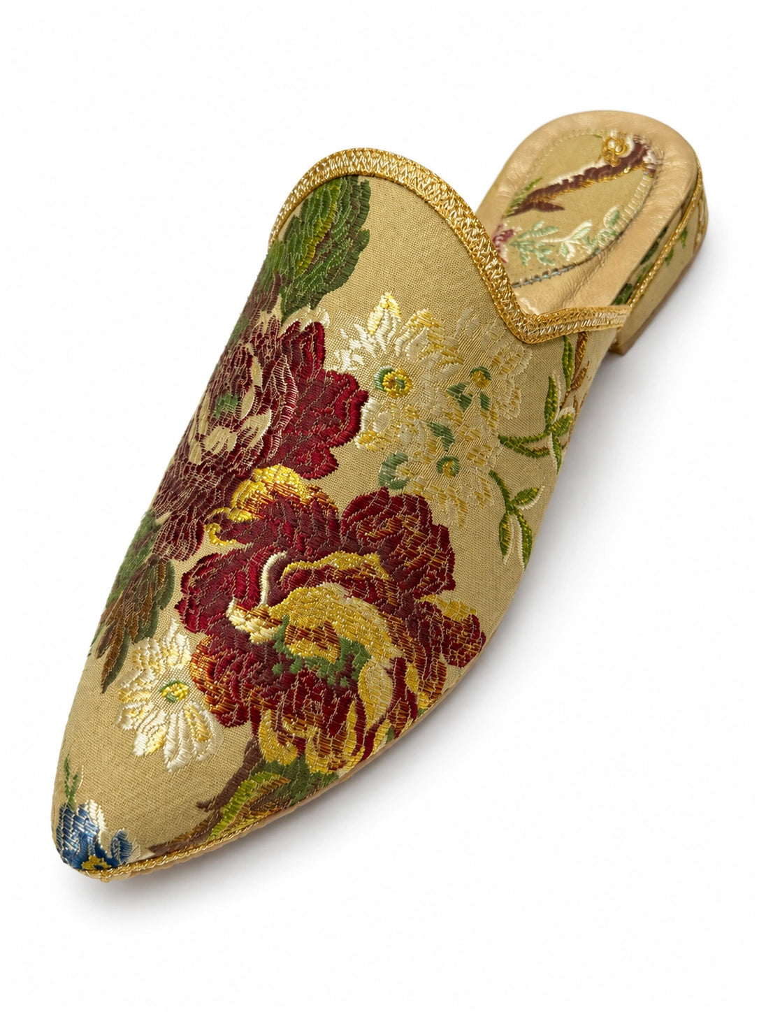 Babouche with burgundy flowers, green leaves and gold-tone details on a light background, with a pointed toe, shown on white.