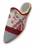 Grey babouche with pink floral motifs, burgundy braided bands and a plain grey pointed toe, shown on white.