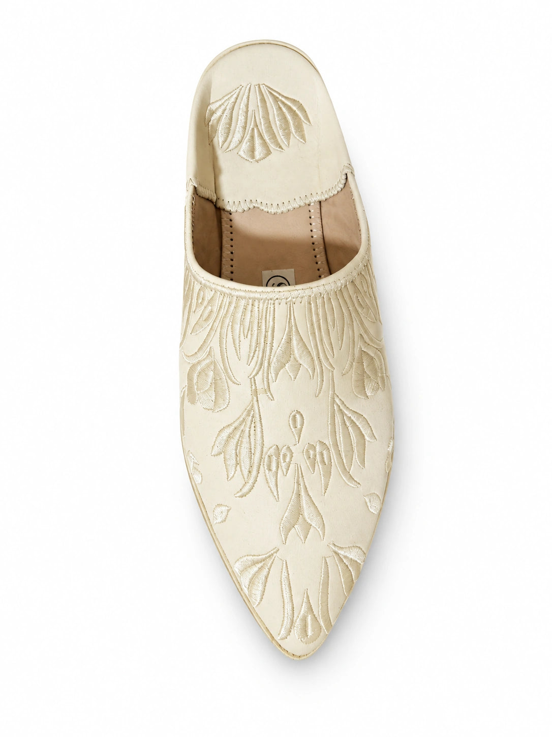 Ivory babouche with tonal floral and leaf motifs and a pointed toe on a white background.