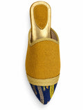 Mustard babouche with a navy blue patterned pointed toe, gold-tone braided band and open back, shown on white.