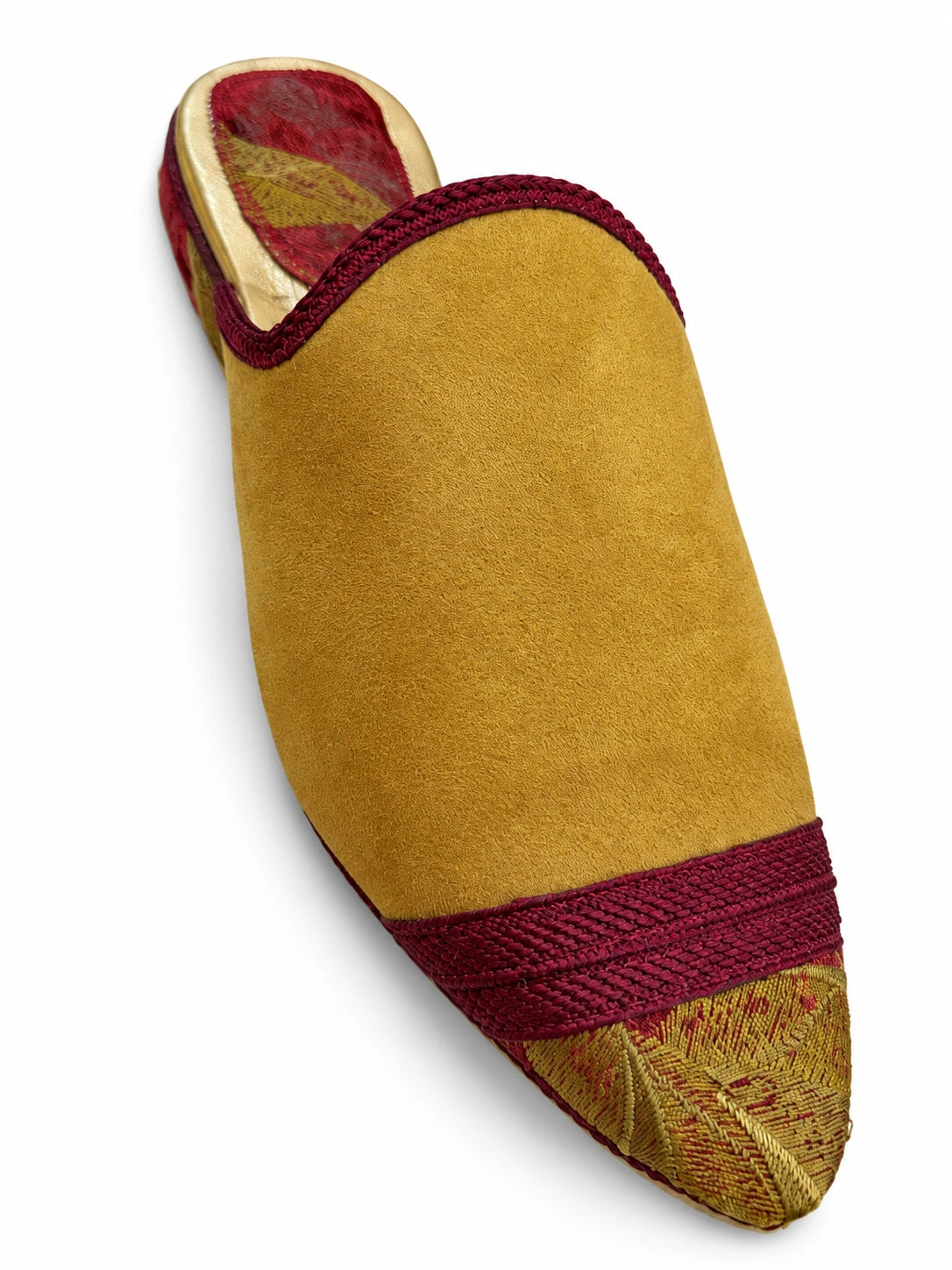 Mustard babouche with a burgundy braided band and leaf-patterned pointed toe on a white background.