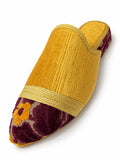 Mustard yellow babouche with a burgundy floral pointed toe, gold-tone braided band and open back on white.