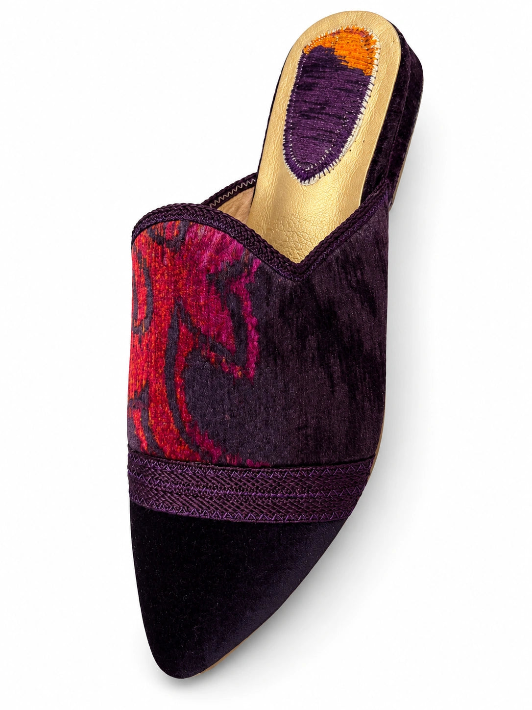Purple babouche with a red and magenta patterned upper, purple braided band and dark pointed toe on a white background.