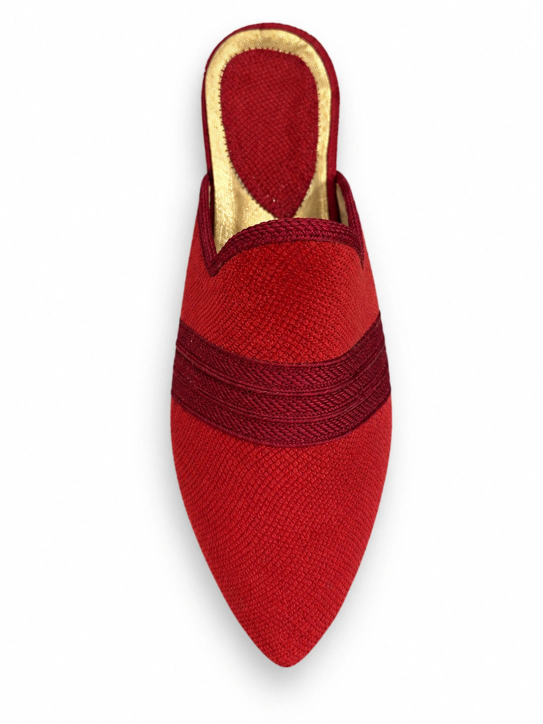 Red babouche with a burgundy braided band and pointed toe on a white background.