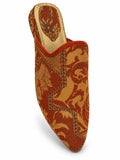Rust and gold floral babouche with olive green detailing and orange braided edging on a white background.